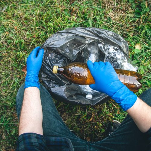 A man cleans up the forest, throws a bottle into a trash bag, close-up. A man puts a plastic bottle in a garbage bag, the concept of forest cleaning and love for nature.